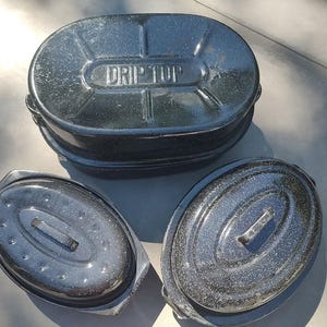 May include: Three black enamel roasting pans. The largest pan has the words "Drip Top" printed on the lid.