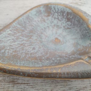 May include: A vintage ashtray with a unique leaf shape. The ashtray features a distressed finish with a blend of gold and teal colors. The design includes a built-in rest for cigarettes.
