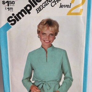 May include: Simplicity sewing pattern for a teal blouse with a mandarin collar and a tie belt. The pattern is for beginner sewers and is level 2. The pattern is for size 12.