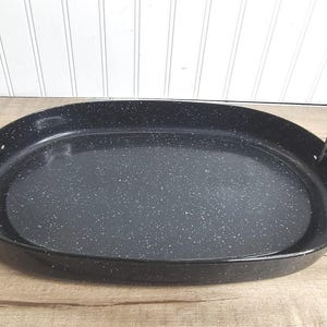 May include: Oval black enamel roasting pan with speckled white accents. Features two metal handles for easy transport. A classic kitchenware item for baking and roasting.
