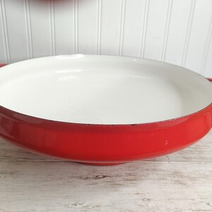 May include: Red enamel cast iron Dutch oven with white interior and two handles.