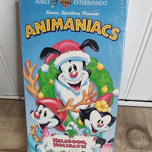 May include: A VHS tape of Animaniacs, a cartoon series, with a blue background and the words "Family Entertainment" and "Steven Spielberg Presents." The cover features cartoon characters in holiday attire, with the text "Helloooo, Holidays!"