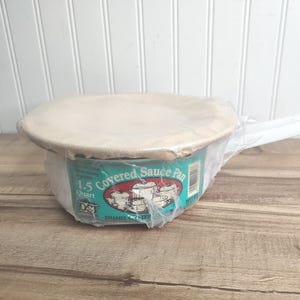 May include: A 1.5-quart covered sauce pan in its original packaging. The pan is teal with a white lid and a long white handle. The packaging includes the words "Covered Sauce Pan" and a graphic of sauce pans.