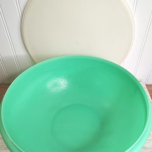 May include: A vintage green mixing bowl with a matching off-white lid. The bowl is a vibrant shade of green, and the lid is a soft, creamy color. The bowl and lid are made of a durable material, perfect for kitchen use.