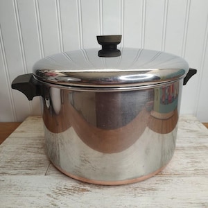 May include: A silver and copper pot with a lid and black handles. The pot has a shiny finish and a copper band around the bottom.