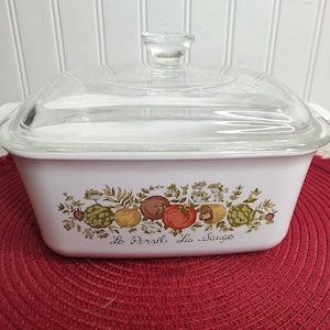 May include: White ceramic casserole dish with a glass lid. The dish has a floral design with green leaves, red tomatoes, and brown mushrooms. The text "Le Persil, La Sauge" is printed on the dish.