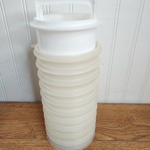 May include: A white, collapsible water carrier with a handle. The carrier is made of a translucent, ribbed material and has a white lid and handle. The container is designed to expand and contract for easy storage and transport.