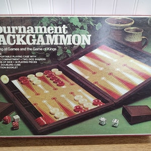 May include: A vintage Tournament Backgammon game set in a brown wooden case with a cork board game surface. The box features the text "Tournament Backgammon" and "The King of Games and the Game of Kings". The game includes two dice shakers, two pairs of dice, 30 playing pieces, and an official doubling cube.