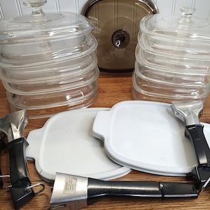 May include: A set of vintage CorningWare cookware with glass lids and white lids with black handles. The cookware is in a stack and includes a brown glass lid.