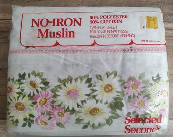 May include: A twin flat sheet in a plastic package. The sheet is white with a floral pattern of yellow and pink daisies and green leaves. The package reads "NO-IRON Muslin" and "50% Polyester 50% Cotton".