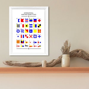 May include: A white framed poster with the title "International Maritime Signal Flags". The poster shows a chart of 26 flags representing the letters of the alphabet, 10 flags representing the numbers 0-9, and an anchor symbol.
