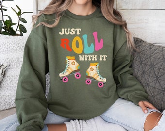 May include: A green sweatshirt with the text "Just Roll With It" in colorful letters. The sweatshirt features a graphic of two vintage roller skates with floral accents.