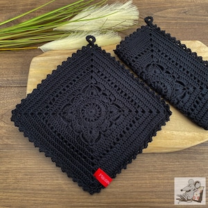 May include: Two black crocheted pot holders with a floral design. The pot holders have a loop for hanging. The larger pot holder has a red label with the word "Mauser" on it.