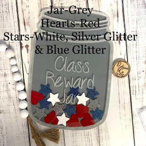 May include: A grey mason jar with a white, silver, and blue glitter design. The jar has red hearts and white stars inside. The jar says "Class Reward Jar" on the front.