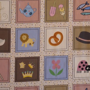 Op de afbeelding: Een stofpatroon met een raster van vierkanten, elk met een andere illustratie. De afbeeldingen omvatten een kat, theepot, ijs, vis, eend, leeuw, pretzel, hoed, lolly, kronen, bloem en lieveheersbeestje.