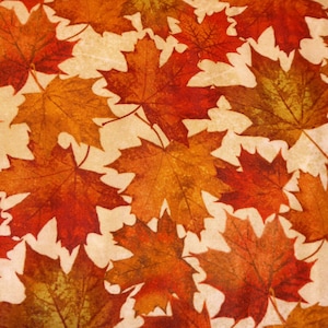 Könnte beinhalten: Nahaufnahme eines Stoffes mit einem sich wiederholenden Muster aus Herbstahornblättern. Die Blätter sind in Rot-, Orange- und Gelbtönen gehalten und haben ein strukturiertes Aussehen. Der Hintergrund ist hellbeige. Das Gesamtthema ist Herbst und Natur.