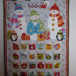 Może przedstawiać: Materiałowy kalendarz adwentowy z bałwanami, pingwinami i prezentami świątecznymi. Kalendarz ma 24 ponumerowane kieszenie z świątecznymi ilustracjami. U góry zielone pętle do zawieszenia.