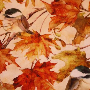 Op de afbeelding: Stofafdruk met een aquarelontwerp van herfstbladeren in tinten oranje, geel en bruin. Twee kleine vogels met zwart-witte koppen zitten op takken tussen de bladeren.