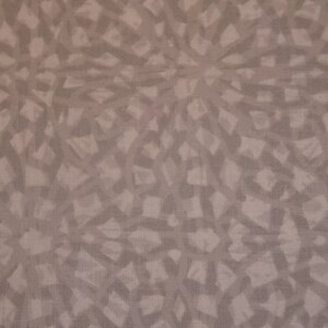 May include: A beige fabric with a repeating pattern of abstract shapes. The shapes are a light brown color and are arranged in a radial pattern.