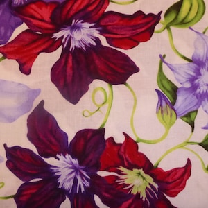 Può includere: Un tessuto bianco con un motivo floreale con fiori viola, rossi e verdi. I fiori sono stilizzati e hanno un aspetto pittorico.