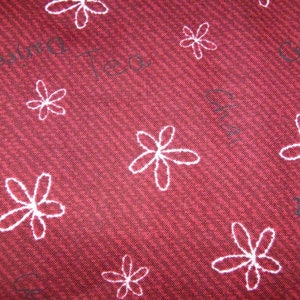 Könnte beinhalten: Nahaufnahme eines roten Stoffes mit diagonal gerippter Textur. Weiße Umrissblumenmuster sind über die Oberfläche verstreut. Schwacher Text, einschließlich des Wortes "Tea", ist sichtbar.