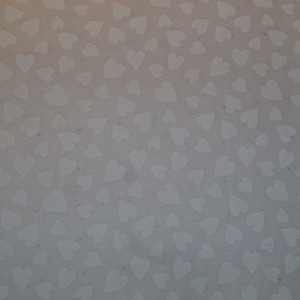 Pode incluir: Um tecido branco com um padrão repetitivo de pequenos corações brancos sobre um fundo cinza claro.