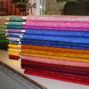 May include: A stack of colourful fabric rolls in various shades of pink, blue, yellow, red, and brown. The fabric has a mottled, tie-dye effect.