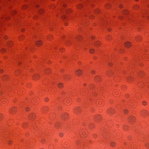 Op de afbeelding: Rode stof met een herhalend patroon van donkerbruine cirkels en swirls.