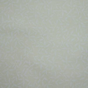 May include: A close-up of a light beige fabric with a white floral pattern. The fabric has a subtle texture and a soft, delicate look.