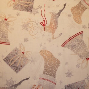 Op de afbeelding: Een witte stof met een herhalend patroon van zilveren bellen, rendieren en kousen. Het patroon is op een crèmekleurige achtergrond met rode accenten.