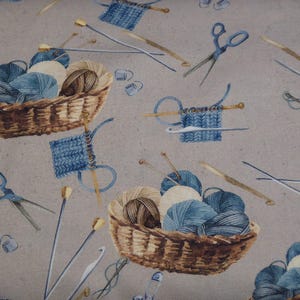 Könnte beinhalten: Ein Stoffmuster mit Körben voller Garn in Blau-, Braun- und Cremetönen, zusammen mit Stricknadeln, Scheren und gestrickten Quadraten. Das Design hat einen Aquarelleffekt mit einem neutralen grauen Hintergrund.