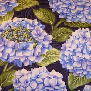 Op de afbeelding: Een close-up van een stof met een herhalend patroon van blauwe en paarse hortensia's op een donkerblauwe achtergrond. De hortensia's worden omringd door groene bladeren.