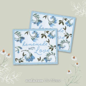 Pode incluir: Duas etiquetas de tecido azul e branco com um padrão floral e o texto "homemade with love". As etiquetas estão sobre um fundo bege claro.