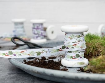 Pode incluir: Um carretel de fita branca com uma estampa floral e vegetal. A fita apresenta um desenho de cenouras, ervas e outros vegetais de jardim. O carretel é de madeira e tem um acabamento branco.