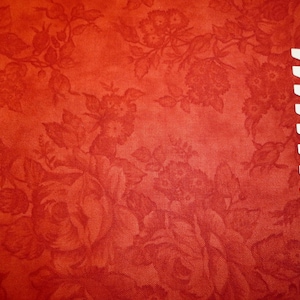 May include: Red fabric with a floral pattern. The fabric has a subtle texture and a slightly faded look. A white ruler is visible in the bottom right corner of the image.
