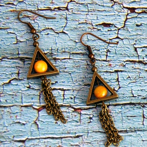 May include: A pair of gold-toned triangle earrings with a dangling chain and a yellow bead in the center of each triangle.