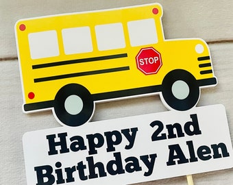 May include: A yellow school bus cake topper with a white sign that says "Happy 2nd Birthday Alen".