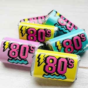 Pu&ograve; includere: Primo piano di sei piccoli dolci avvolti con sfondo rosa, giallo e blu. Ogni dolce ha un fulmine e il testo "80's" in lettere nere e rosa.