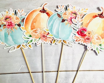 May include: Four watercolour pumpkin toppers with floral arrangements. The pumpkins are in shades of orange and teal, with detailed floral accents in pink, peach, and yellow. Each pumpkin is attached to a wooden stick, ideal for cake decorating or autumn crafts.