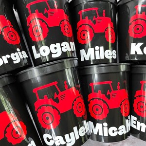 May include: Black plastic cups with red tractor designs and names printed on them, including Georgia, Logan, Miles, Kole, Caylee, Micahl, and Emery.