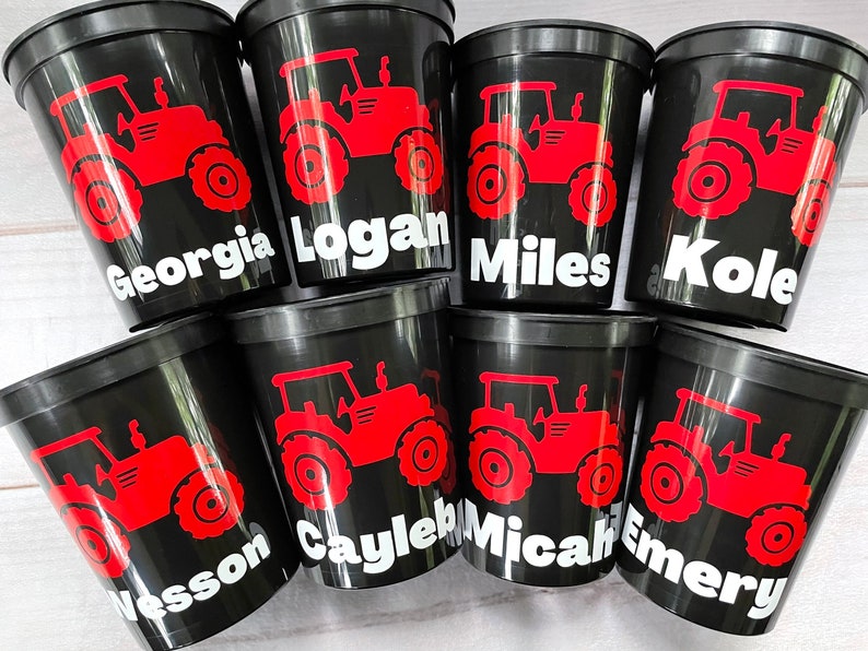 May include: Eight black plastic cups with red tractor designs and white names on each cup. The names are Georgia, Logan, Miles, Kole, Wesson, Cayleb, Micah, and Emery.