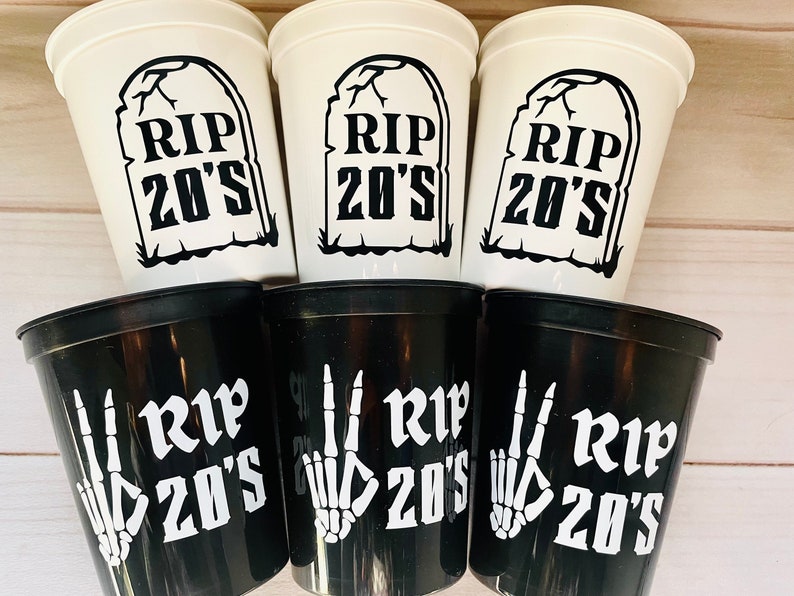 Pu&ograve; includere: Sei bicchieri di plastica, tre bianchi e tre neri, con il testo "RIP 20's" su ciascuno. I bicchieri bianchi hanno un'immagine di una lapide, mentre i bicchieri neri hanno un'immagine di una mano scheletrica.