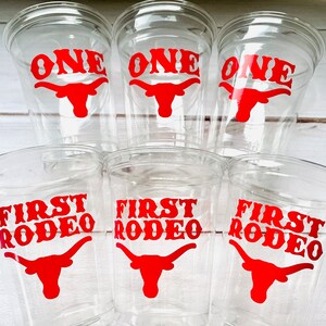 K&ouml;nnte beinhalten: Sechs durchsichtige Plastikbecher mit roten Vinyl-Aufklebern. Drei Becher sagen "ONE" mit einem roten Stierkopf. Drei Becher sagen "FIRST RODEO" mit einem roten Stierkopf.