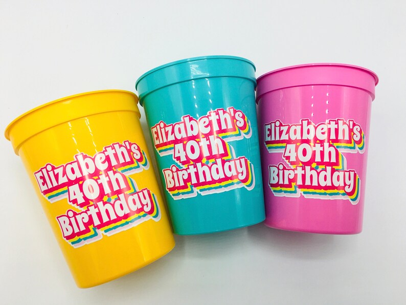 Puede incluir: Tres vasos de pl&aacute;stico de colores: amarillo, turquesa y rosa. Cada vaso tiene el texto "Elizabeth's 40th Birthday" en una fuente retro. Ideales para una fiesta.