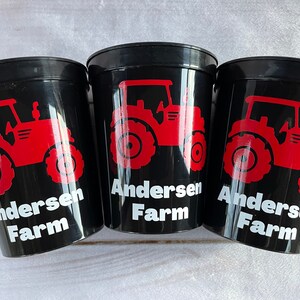 May include: Three black plastic cups with red tractor designs and the text "Andersen Farm" in white.