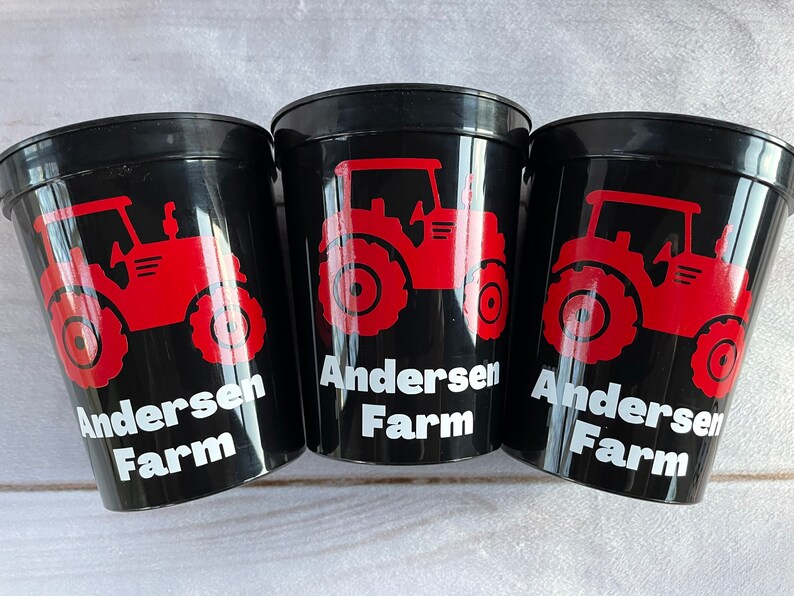 May include: Three black plastic cups with red tractor designs and the text "Andersen Farm" in white.