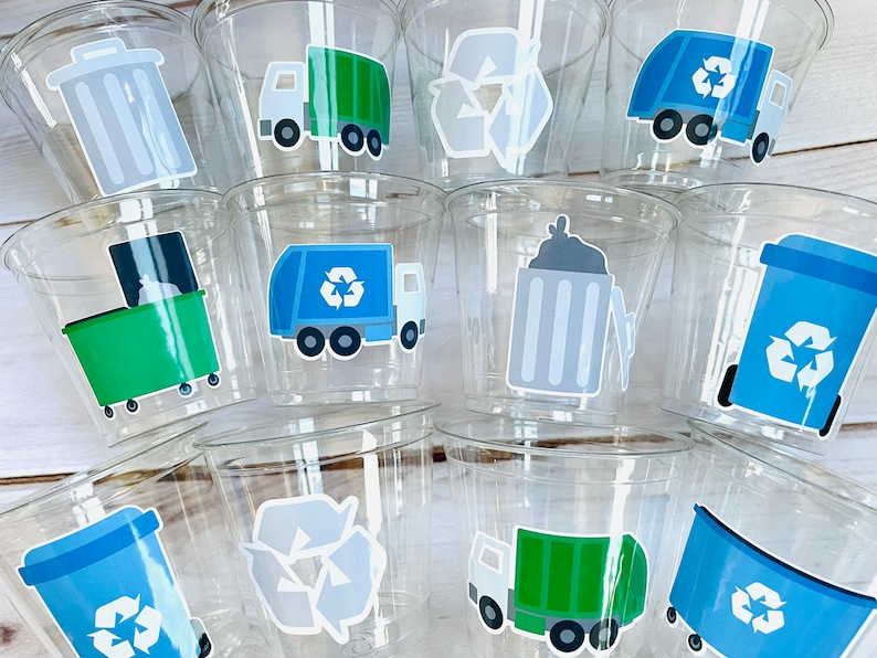 May include: A set of clear plastic cups with various recycling themed stickers. The stickers feature a green recycling bin, a blue recycling bin, a gray recycling bin, a green garbage truck, a blue garbage truck, and a recycle symbol.