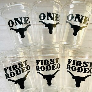 K&ouml;nnte beinhalten: Sechs durchsichtige Plastikbecher mit schwarzen Vinyl-Aufklebern. Drei Becher sagen "ONE" mit einer schwarzen Silhouette eines Longhorn-Rinds. Drei Becher sagen "FIRST RODEO" mit einer schwarzen Silhouette eines Longhorn-Rinds.