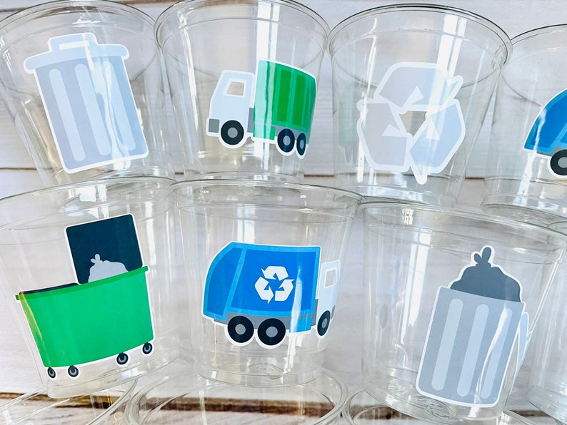 May include: Clear plastic cups with various recycling themed stickers. The stickers feature a trash can, a recycling truck, a recycling symbol, and a garbage bag.