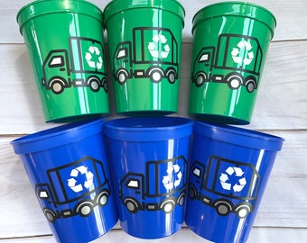 May include: Six plastic cups, three green and three blue, are arranged in a group. Each cup features a black and white graphic of a recycling truck with a recycling symbol on the side.